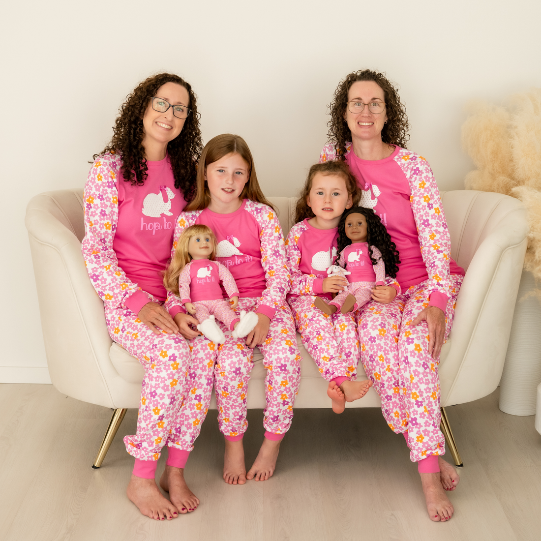 Two mothers, two daughters and two dolls are all wearing matching pajamas with a rabbit theme.