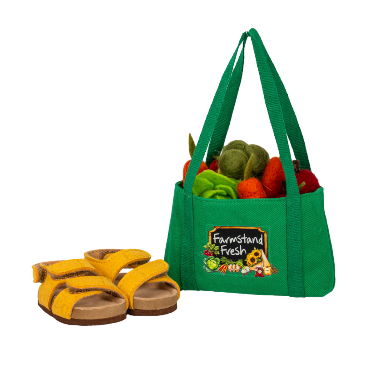 A green fabric tote bag filled with colourful felt vegetables, shown next to a pair of yellow felt sandals on a plain white background. The bag has a front patch that reads 'Farmstand Fresh'.