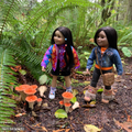 Two 18-inch dolls standing in a forest wearing colourful sweaters and outfits with orange mushrooms and ferns.