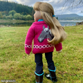 18-inch doll wearing a pink sweater with a horse design in a grassy field with a lake and trees.