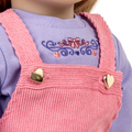 Close-up of a 18-inch doll wearing pink overalls with heart buttons on a purple shirt.