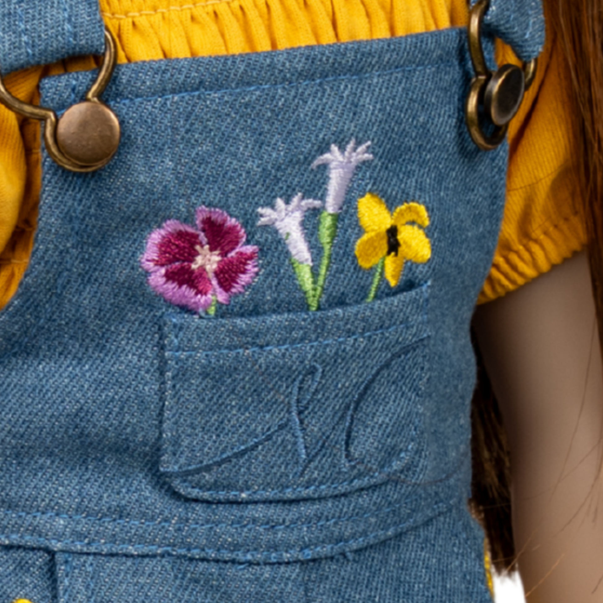 Close-up of denim overalls with embroidered flowers coming out of the front pocket.