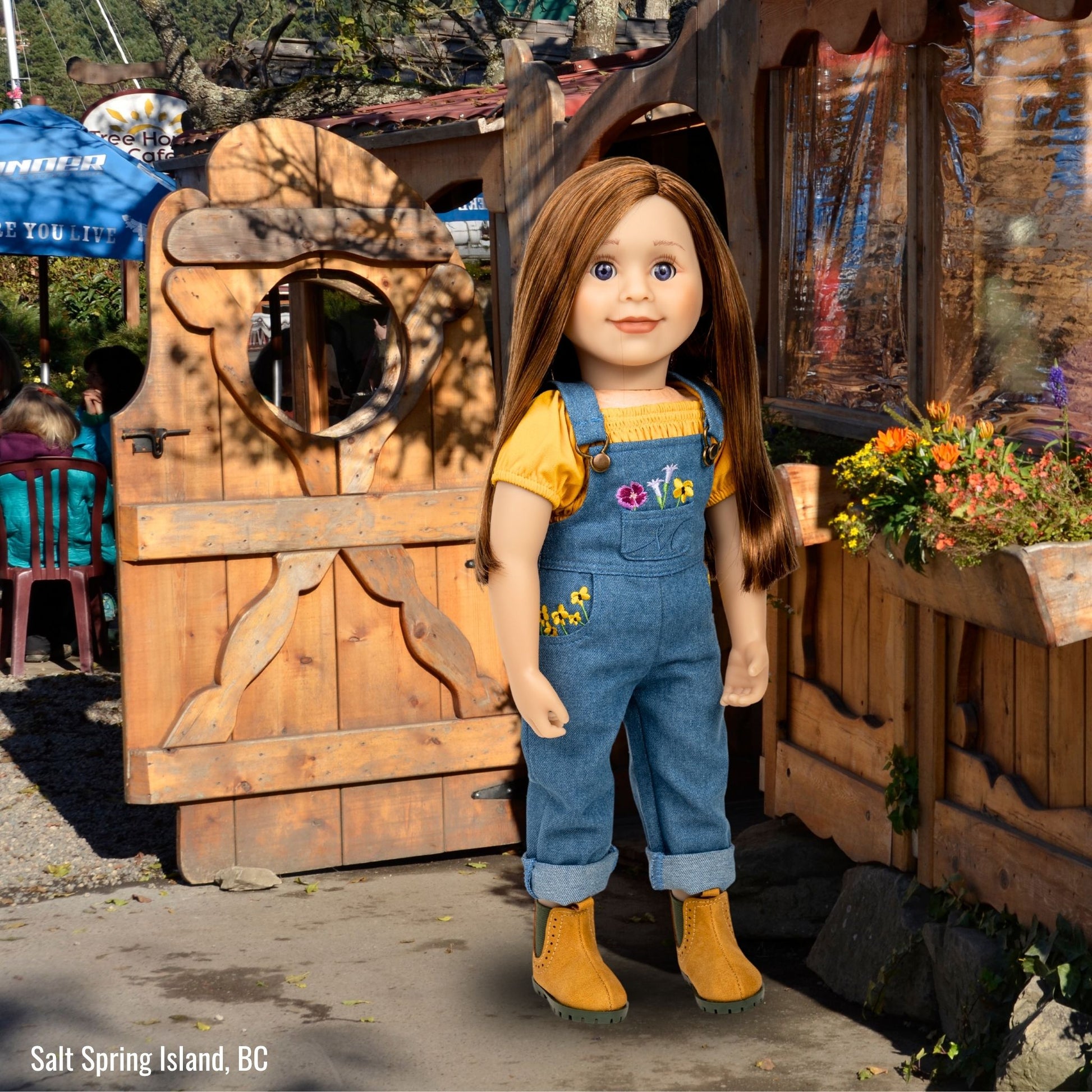 Charlsea doll wearing embroidered overalls in front of carved door at the Tree House Cafe in Salt Spring Island BC