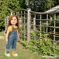 Charlsea doll wearing Bloomin Overalls in front of an artistic fence on Salt Spring Island, BC.