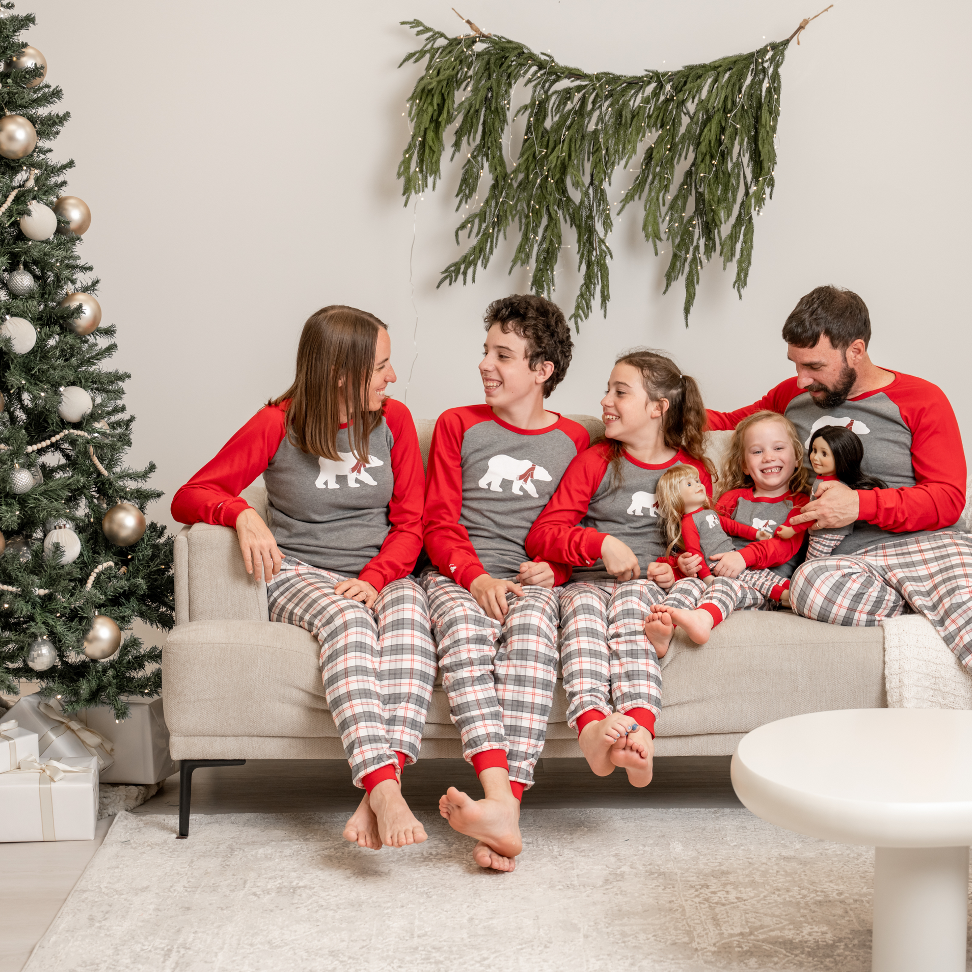 Family sitting on a couch wearing matching polar bear plaid pajamas in a festive christmas living room.
