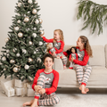 Children in matching polar bear plaid pajamas sitting on a couch with 18-inch dolls next to a decorated Christmas tree.