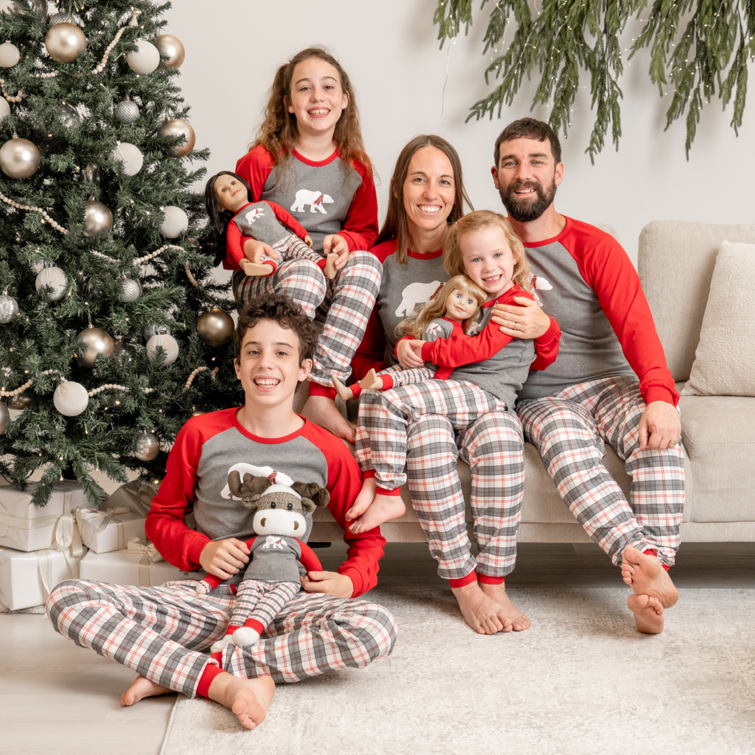 Family in matching plaid polar bear pajamas sitting on a couch with a decorated Christmas tree in the background.