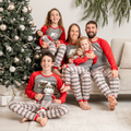 Family in matching plaid polar bear pajamas sitting on a couch with a decorated Christmas tree in the background.