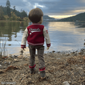 18-inch doll in a red and white varsity jacket standing by a lake with mountains in the background.