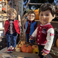 Three 18-inch dolls in autumn-themed outfits with pumpkins in a wooden cart.
