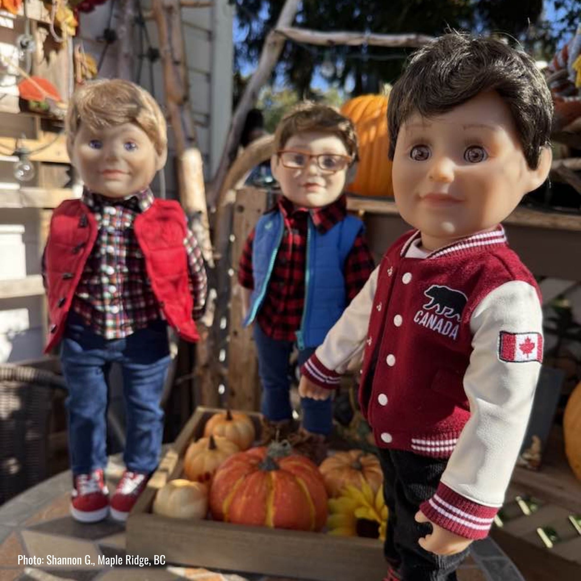 Three 18-inch dolls in autumn-themed outfits with pumpkins in a wooden cart.