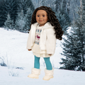 18-inch doll in winter clothing and white boots standing in a snowy landscape with trees.