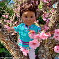 Diverse boy doll wearing knit vest sitting in a cherry tree.