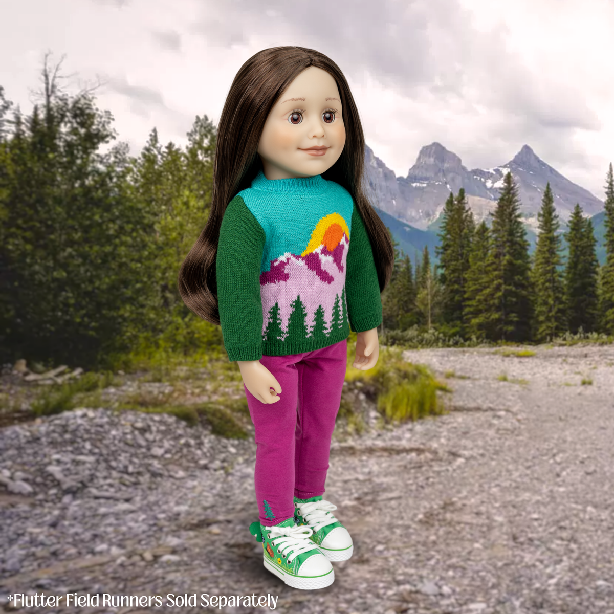 A doll with long brown hair stands outdoors in front of mountains and trees, wearing a colorful knit sweater with green sleeves and a mountain-and-sun graphic, bright pink pants, and green-and-white sneakers. Text at the bottom reads 'Flutter Field Runners Sold Separately. Taryn Maplelea doll outdoor jumper knit sweater for 18 inch dolls, 