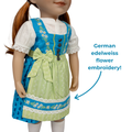 A doll wearing a traditional German dirndl dress with a bright blue bodice, pale green skirt, white lace sleeves, and embroidered white flowers. Text on the right reads 'German edelweiss flower embroidery!' with an arrow pointing to the skirt embroidery. Close-up of Edelweiss detailing, lace trim and printed apron on doll dirndl dress
