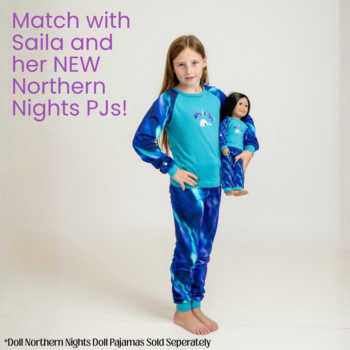 A young girl stands barefoot against a light studio background wearing a blue and turquoise long-sleeve pajama set with a matching patterned pair. She is holding a doll wearing the matching pajamas.