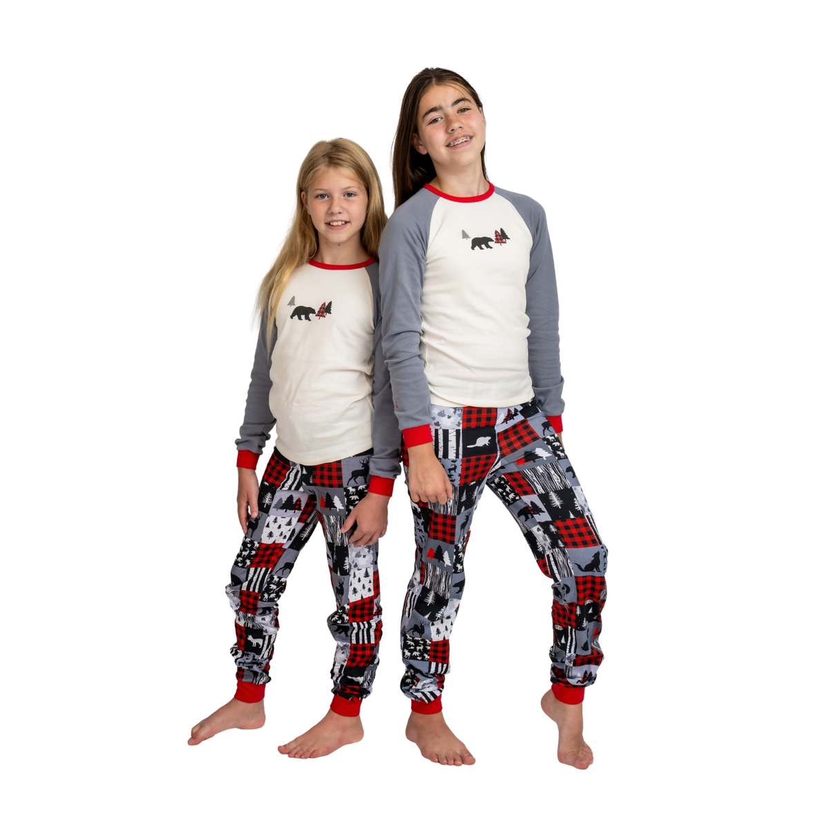 Two children standing barefoot and wearing matching long-sleeve pajamas with cream fronts, gray sleeves, red trim, and patterned pants featuring red, black, gray, and white city-style motifs.