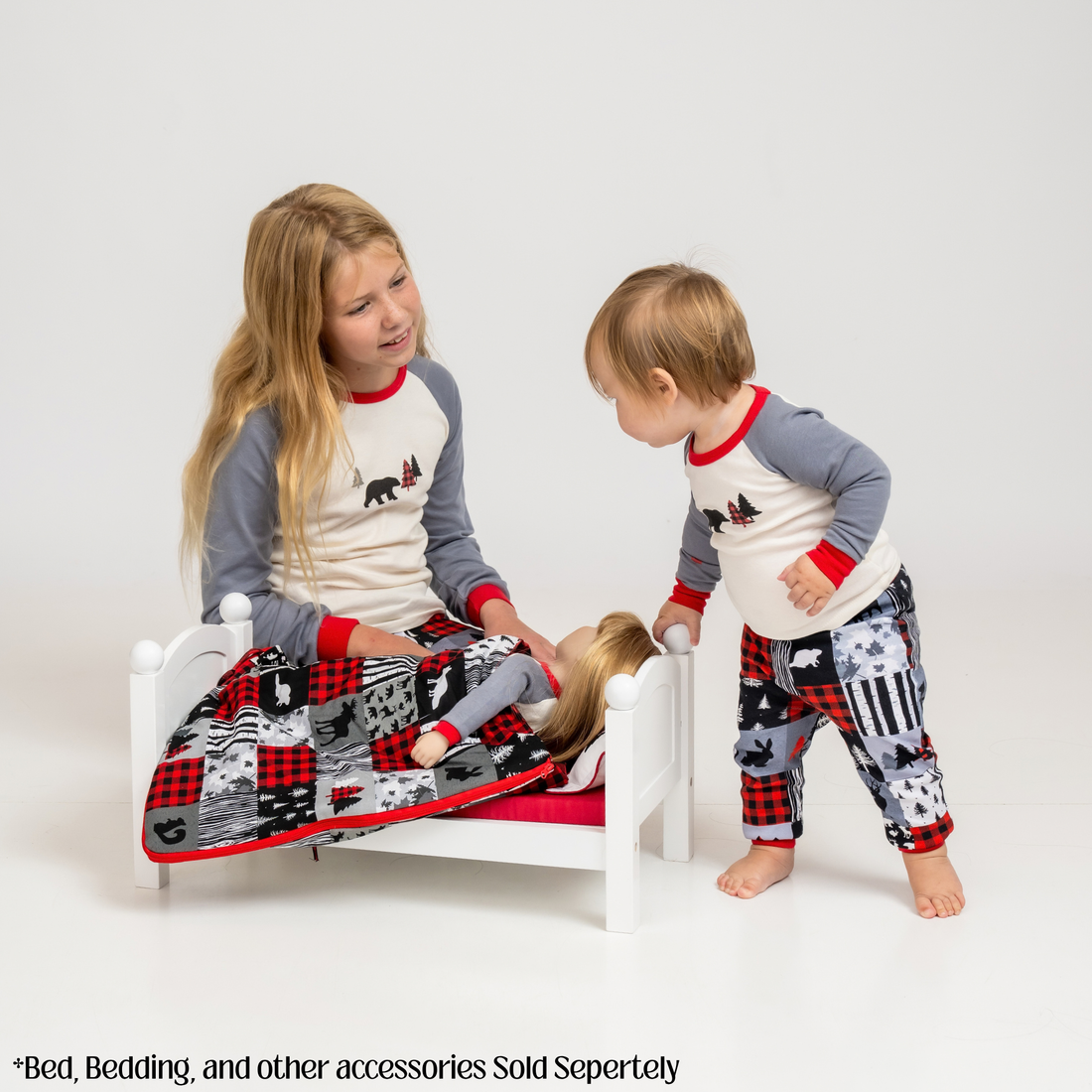 Two children standing barefoot and wearing matching long-sleeve pajamas with cream fronts, gray sleeves, red trim, and patterned pants featuring red, black, gray, and white city-style motifs.