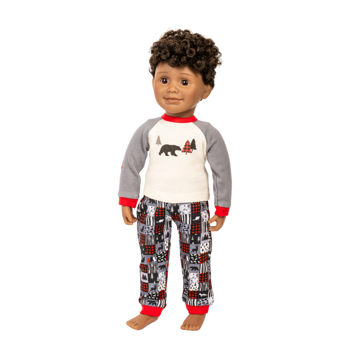 A doll with curly brown hair wearing a two-piece pajama set. The set includes a long-sleeve raglan shirt with a white chest, gray sleeves, red trim, and a bear graphic, paired with matching patterned pants featuring red, black, and gray designs, all on a solid white background.