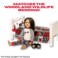 A Maplelea doll wearing a woodland-themed pajama set sits on a white bed frame with a matching red, black, and gray woodland print bedding set. The doll is also wearing black bear slippers.