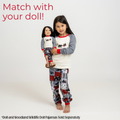 A young girl stands barefoot against a light gray studio background wearing a matching long-sleeve pajama top and patterned pants, while holding a doll in a matching pajama set. Red text at the top reads 'Match with your doll!' and a small disclaimer appears at the bottom.