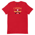 Front view of a red adult T-shirt displayed on a light grey background. The shirt features a Canada-themed graphic with the word “CANADA” in gold above a white maple leaf, a gold canoe, and crossed black paddles. Below the design are the words “TRUE NORTH STRONG & FREE” in white. The shirt has short sleeves and a crew neckline.