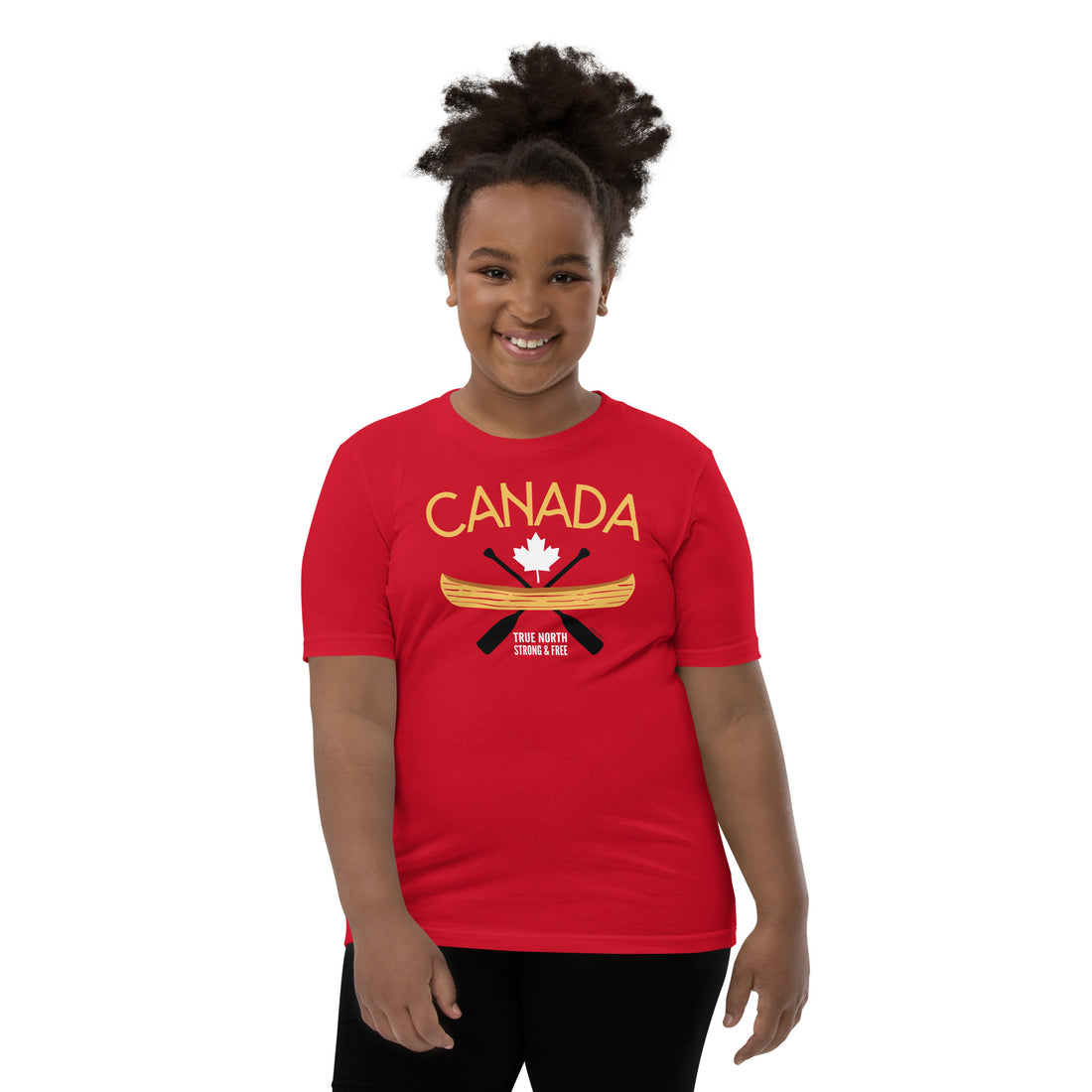 Smiling child wearing a red “Canada” graphic T-shirt against a light gray background. The shirt features a yellow canoe, crossed black paddles, a white maple leaf, and the words “Canada” and “True North Strong & Free.” The child stands facing forward, showcasing the front design of the youth T-shirt.