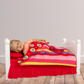 18-inch doll lying on a wooden bed with a red and yellow striped blanket featuring music notes and guitar.