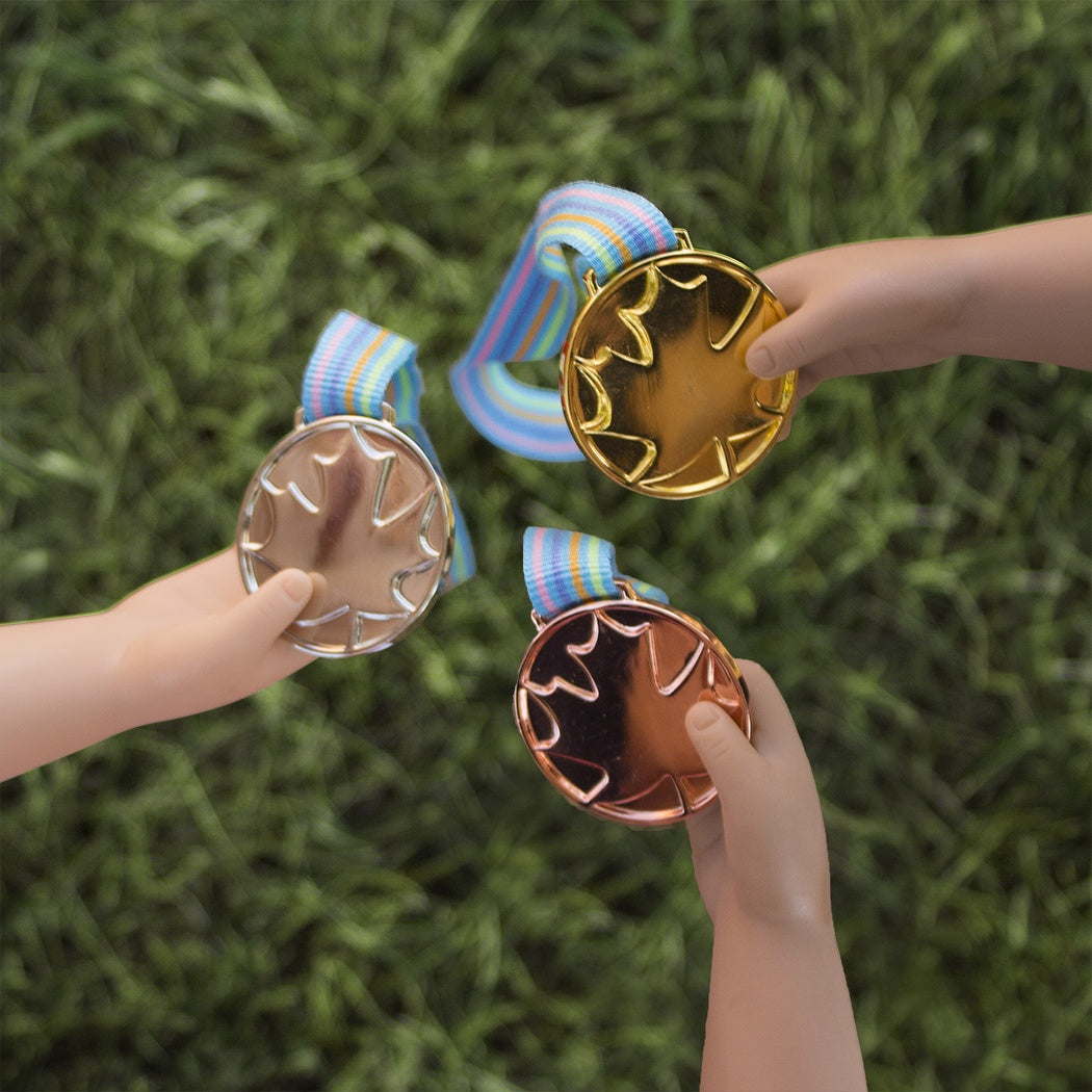 Three doll hands holding gold, silver, and bronze medals from Maplelea Canadian Girl Dolls Winner's Set.
