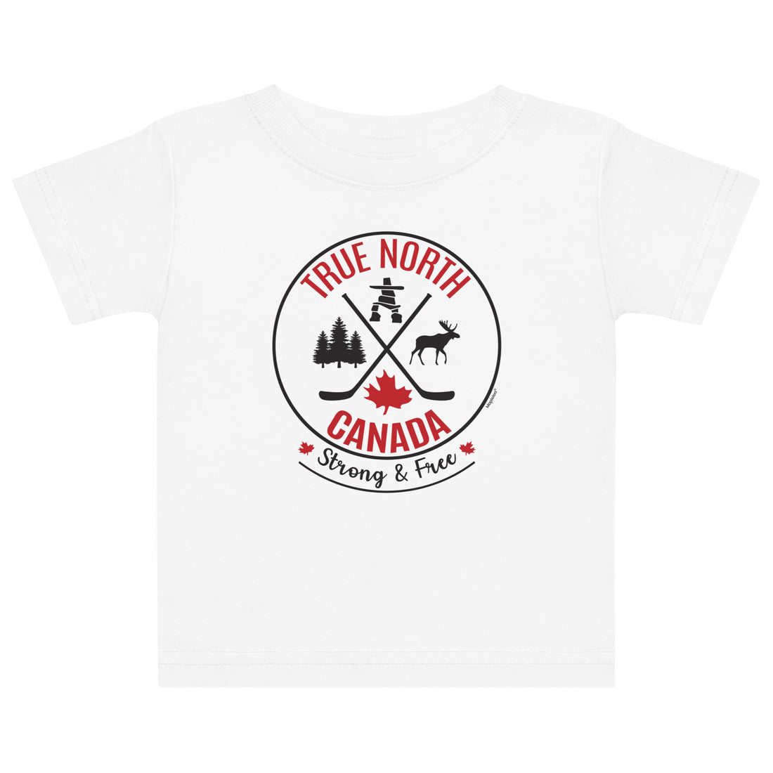 A young child with curly dark hair stands against a light gray background wearing a white T-shirt featuring a circular “True North Canada” graphic with crossed hockey sticks, a maple leaf, and wildlife silhouettes. The child also wears light pink heart-patterned shorts, matching socks, and beige sneakers, looking down with one hand raised near their hair.