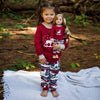 A young girl and doll wearing matching pjs with a winter theme.