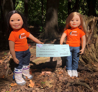 Two Maplelea dolls holding a cheque donating to the Orange Shirt Society