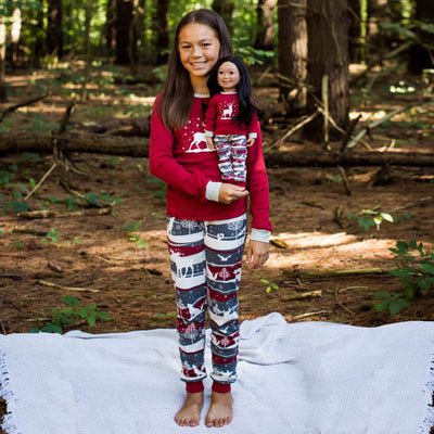 A girl and her doll dress alike in matching pajamas on a forest background.