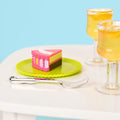 A close up of a slice of the party pieces cake on a plate with a fork in front, and two glasses of lemonade to the right side.